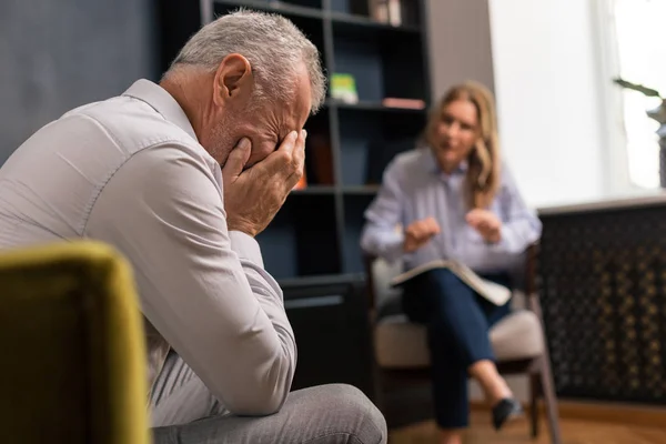 Hombre deprimido de pelo gris cubriéndose la cara con las manos — Foto de Stock