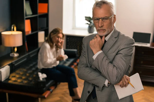 Psicólogo serio atractivo pensando mientras sostiene un bloc de notas — Foto de Stock