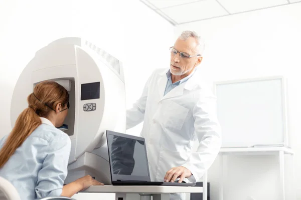 Grey-haired eye specialist wearing glasses standing near patient — Stock Photo, Image