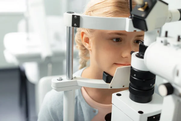 Girl looking into special glasses while having eye sight consultation — Stock Photo, Image