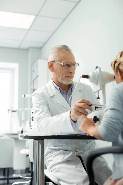 Qualified eye doctor wearing white coat sitting and consulting girl — Stock Photo, Image