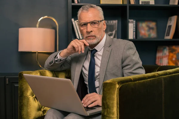 Guapo elegante hombre serio de pelo gris con un ordenador portátil —  Fotos de Stock