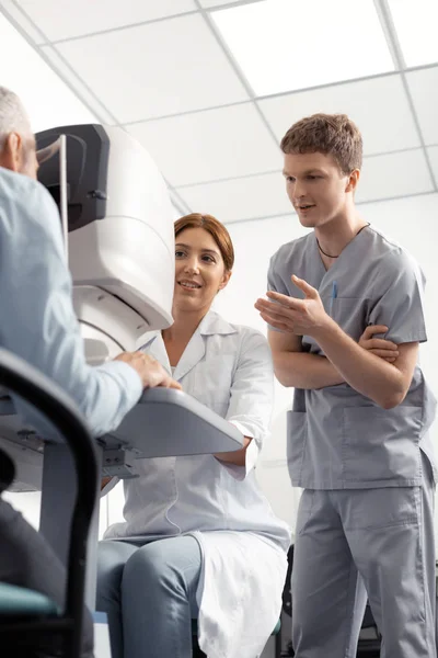 Dark-haired assistant standing near eye doctor during examination — Stock Photo, Image