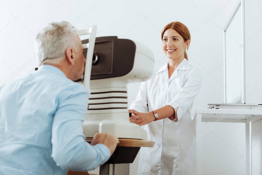 Red-haired eye doctor smiling while analyzing eye sight of patient