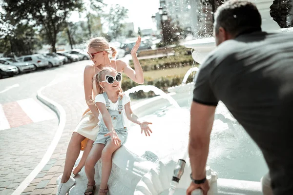 Klein meisje spelen met haar ouders in de buurt van fontein. — Stockfoto