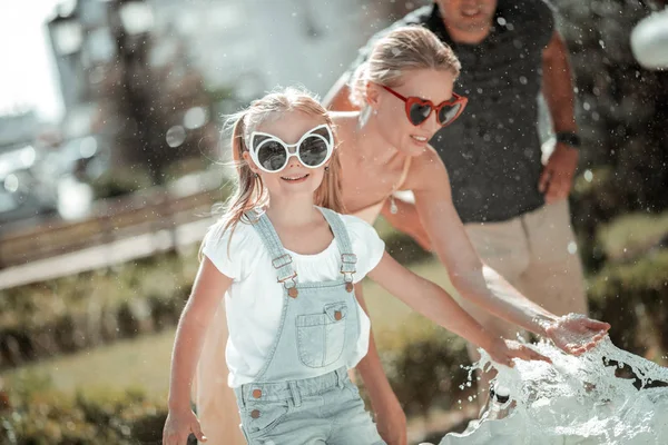 Smiling girl playing with fountain splashes in summer. — Stock Photo, Image