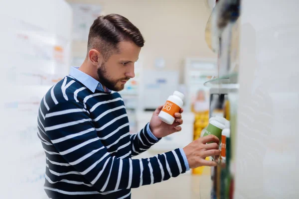 Concentrated young bearded man choosing necessary pills — Stock Photo, Image