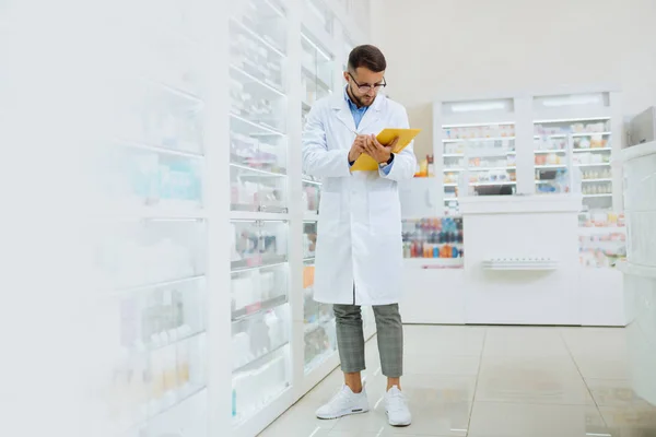 Atento farmacéutico barbudo tomando notas durante la revisión —  Fotos de Stock