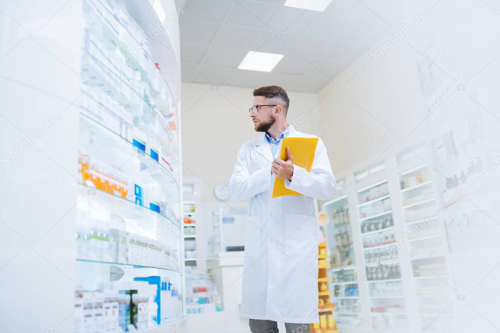 Attentive young brunette apothecary looking at medicine