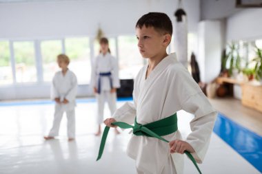 Beyaz kimono giyerken yeşil kuşağını bağlayan koyu saçlı çocuk