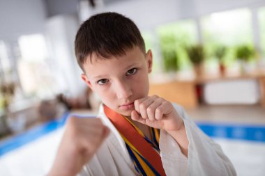 Aikido için kimono giyen koyu saçlı çocuk yumruklarını gösteriyor