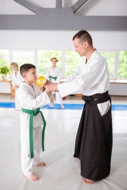 Beyaz kimonolu koyu saçlı çocuk antrenöründen ödül alıyor