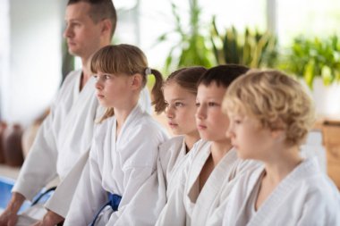 Yerde oturan beyaz kimono giyen çocuklar ve eğitmenleri