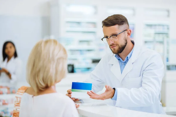 Aufmerksame bärtige Apothekerin demonstriert Packung mit Pillen — Stockfoto