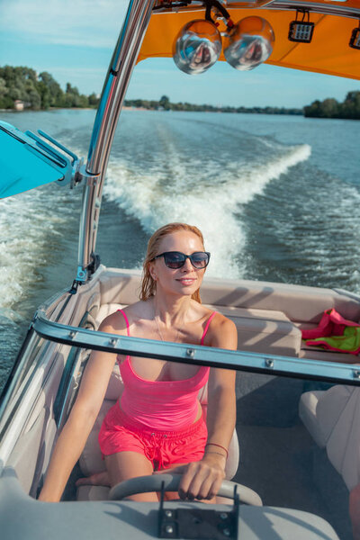 Молодая женщина с светлыми волосами за рулем катера
