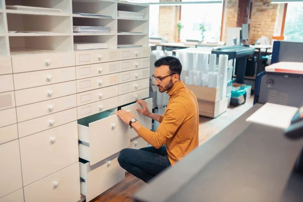 Homem usando óculos à procura de materiais no escritório de impressão — Fotografia de Stock