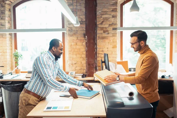 Man working in printing office giving printed books to writer