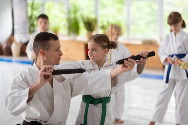 Treinador de aikido de cabelos escuros ajudando menina a usar nunchucks — Fotografia de Stock