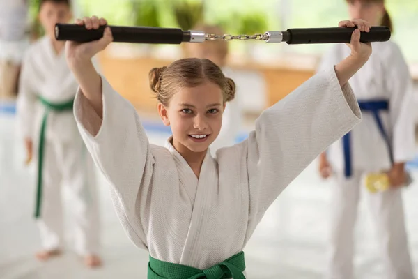 Niña sosteniendo nunchucks mientras practica artes marciales — Foto de Stock