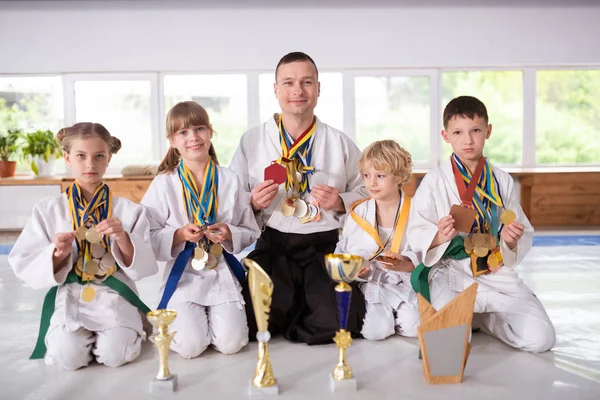 トレーナーの近くに座ってメダルや賞を見せる子供たち — ストック写真
