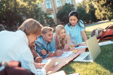 Çimlerin üzerinde yatan ev görevleri üzerinde çalışan öğrenciler.