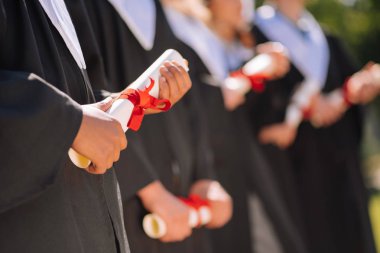 Graduates holding their diplomas in a roll. clipart