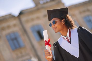 Üniversitenin önünde duran graduand şaşkın.