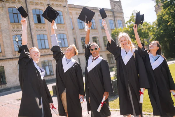 Vrolijke afgestudeerden verhogen hun Masters caps in de lucht. — Stockfoto