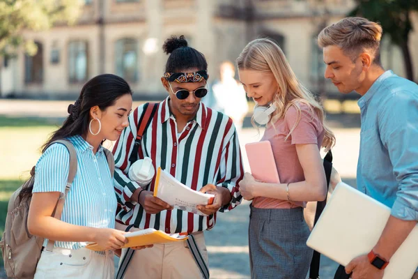 Grup arkadaşlarının dönem ödevlerini okuyan öğrenciler.