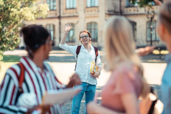 Bahçede grup arkadaşlarına el sallayan gülümseyen çocuk.