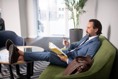 Dizüstü bilgisayar ile masanın yanında otururken işadamı okuma kitap