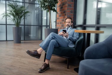 Gri takım elbise giyen işadamı telefonunda e-posta okuyor