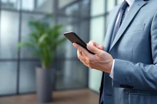Primer plano del hombre de negocios con traje gris sosteniendo teléfono inteligente negro —  Fotos de Stock