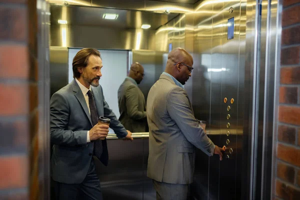站在同事身边时，男子在电梯里按下按钮 — 图库照片
