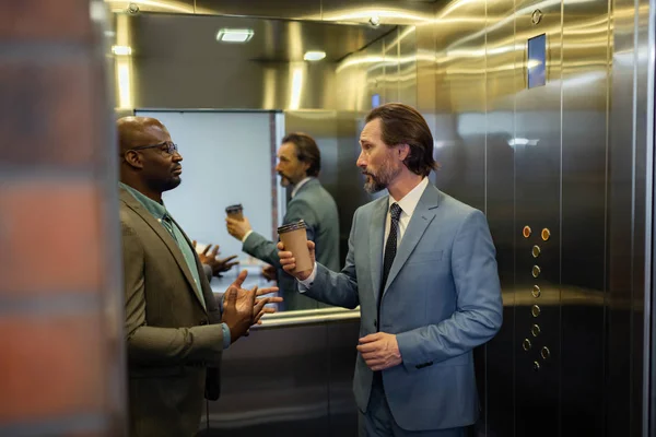 白发男子站在电梯里与同事交谈 — 图库照片