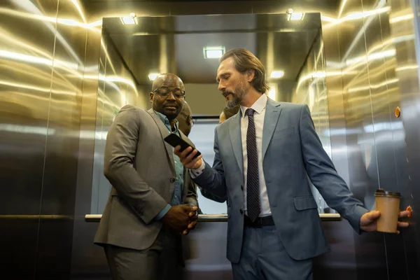 使用电梯时与业务合作伙伴交谈的白发男子 — 图库照片