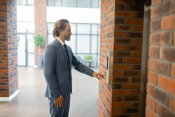 会議後にエレベーターを待つスーツを着た灰色の髪の男 — ストック写真
