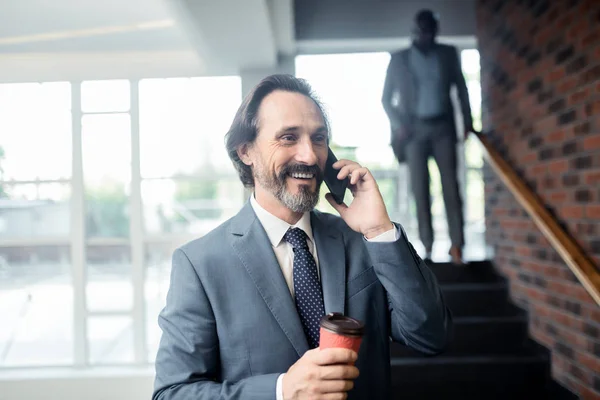 Mężczyzna trzyma kawę uśmiechniętą podczas rozmowy z kolegą — Zdjęcie stockowe