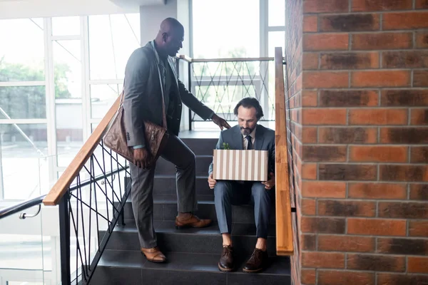 Dark-skinned man calming down his colleague after dismissal