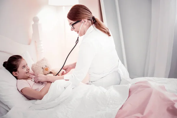 Восхитительный позитивный доктор, сидящий на кровати девочек — стоковое фото