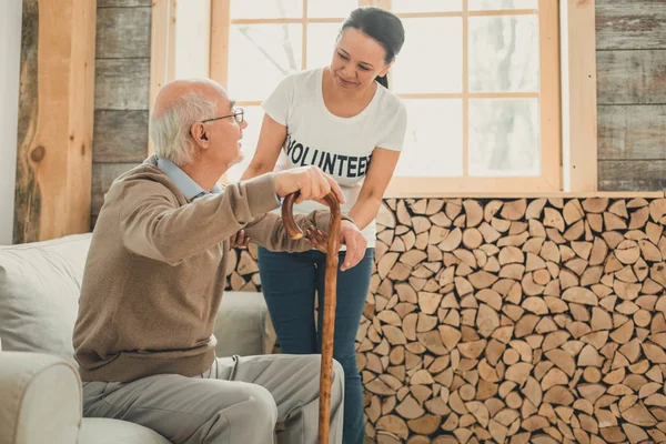 Mujer voluntaria apoyando al anciano levantándose del sofá — Foto de Stock