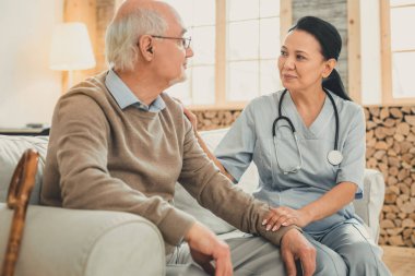 Hemşirelik üniformalı koyu saçlı kadın hastaya yardım ediyor