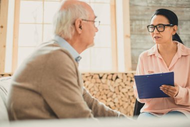 Yaşlı adamla konuşan açık gözlüklü kendinden emin koyu saçlı kadın