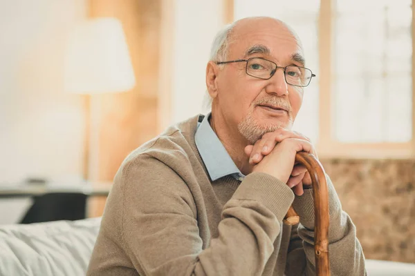 Старий сіроокий чоловік мудро дивиться, сидячи на дивані — стокове фото