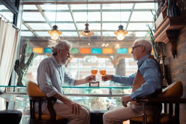 Two retired men clanging their glasses while chilling in pub clipart