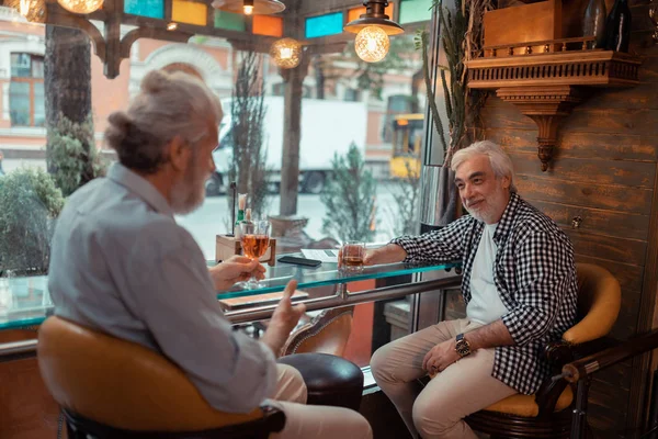 Deux hommes barbus aux cheveux gris qui parlent et boivent de l'alcool — Photo