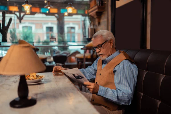 Стильний літній чоловік читає новини та п'є віскі — стокове фото