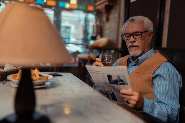 Good-looking man reading newspaper and drinking whisky