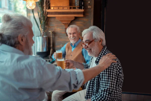 Old friend touching shoulder of man while drinking beer together
