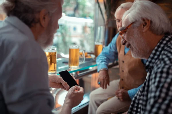 Muž zobrazující smartphone a pití piva s přáteli — Stock fotografie